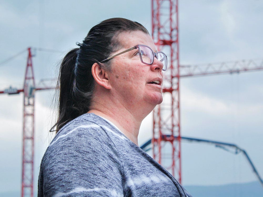 Danielle Pritchett, in a grey shirt and wearing glasses, stands with construction cranes in the background.