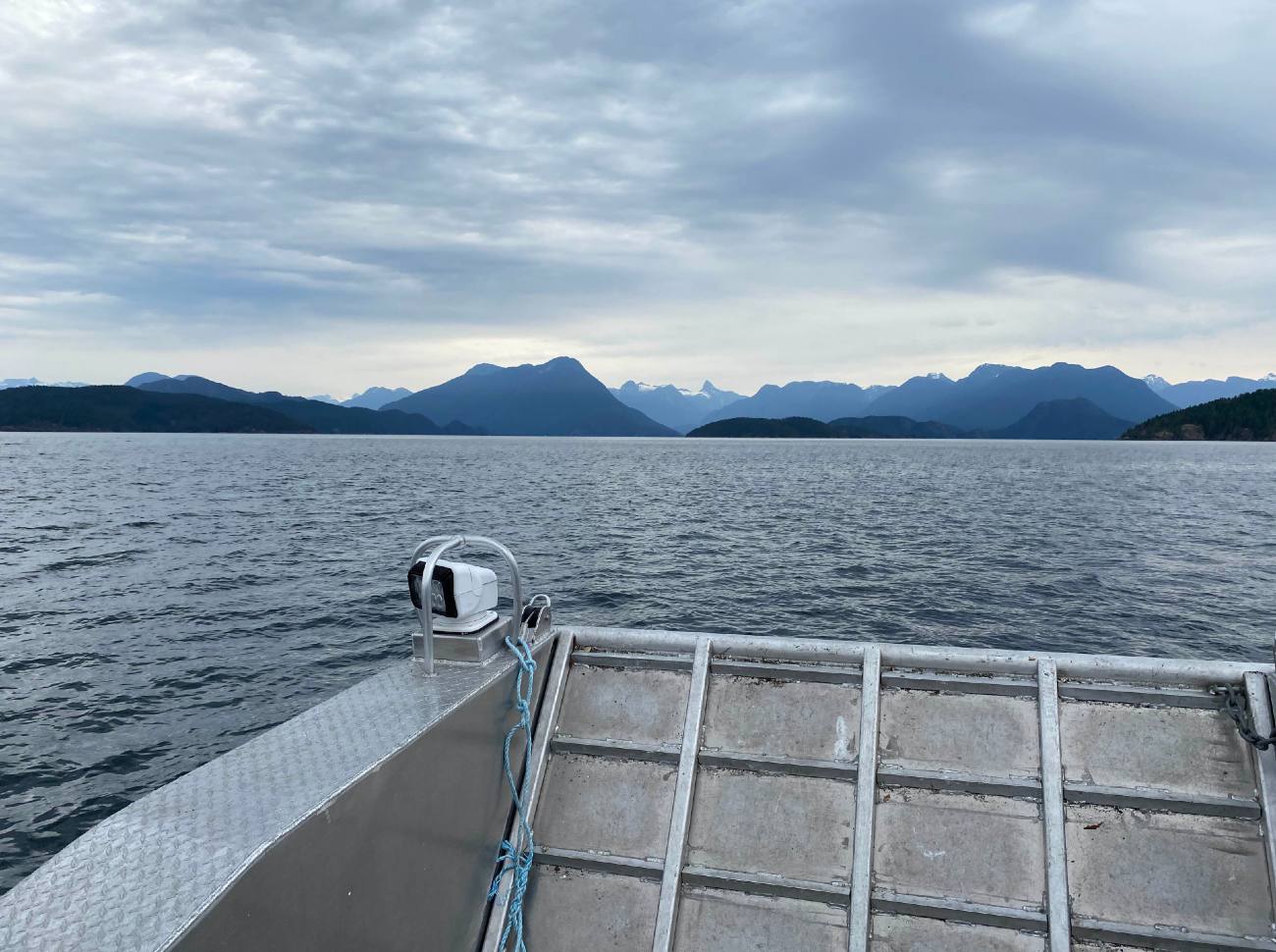 Grey-blue cloudy skies over a big dark blue body of water, with mountains in the background.