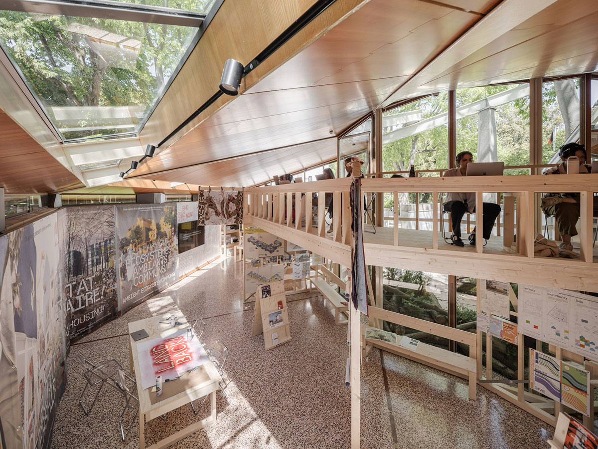 The inside of a bright pavilion with displays and an upper mezzanine made out of plywood. It looks like a fusion of museum-space and classroom. 