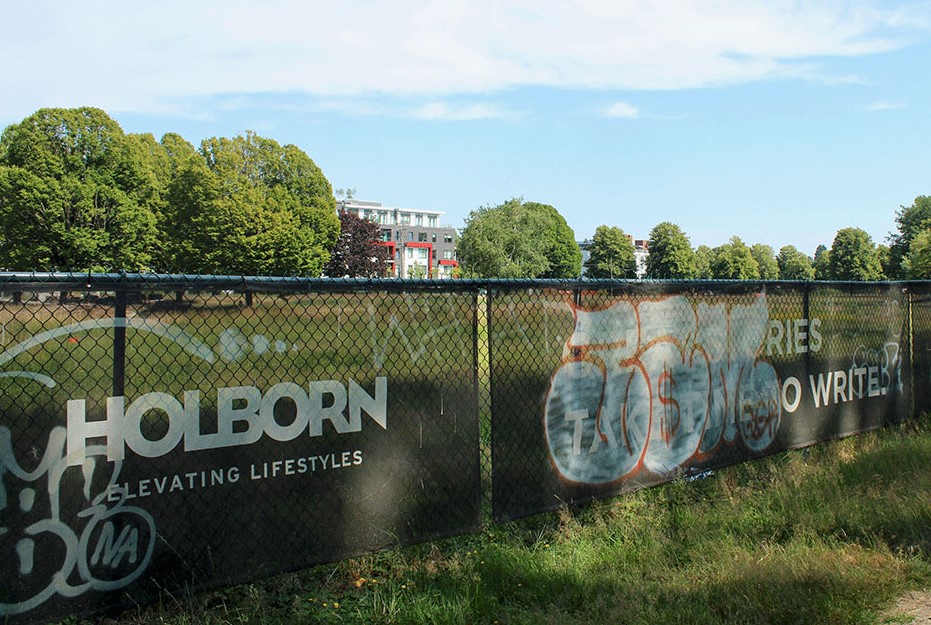 A chain link fence adorned with Holborn advertising banners that say “Great Stories Take Time to Write” and graffiti.