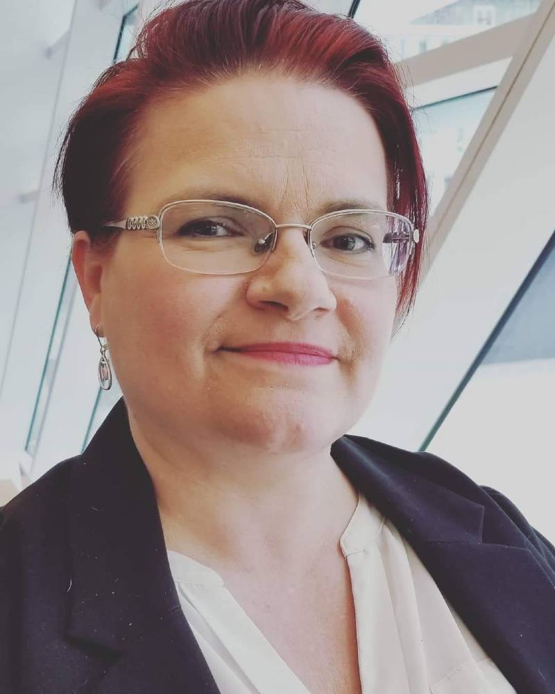 A profile shot of a white woman with short red hair and silver-frame glasses.