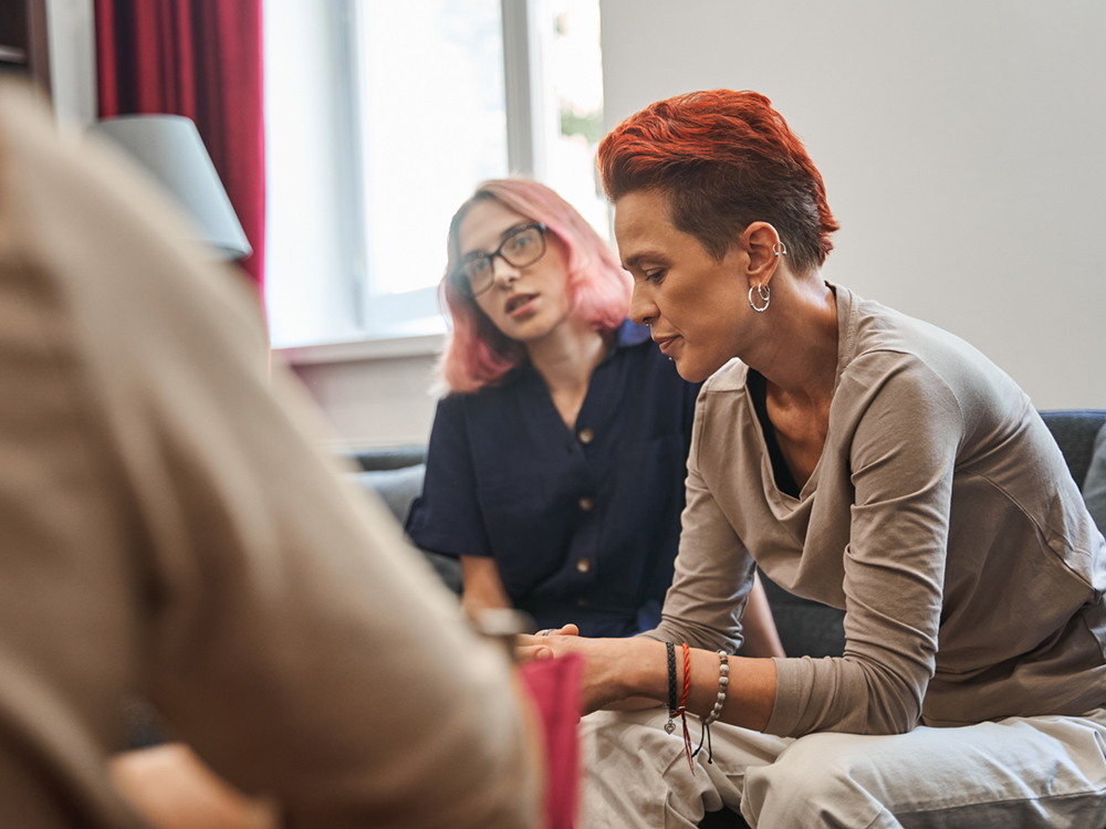A queer couple sits in a doctor&rsquo;s office, speaking to a doctor.
