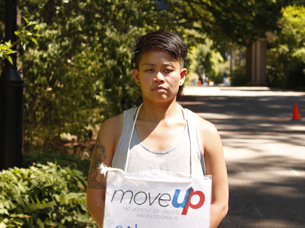 Rose Anza-Burgess, in a tank top and wearing a &ldquo;MoveUP&rdquo; looks at the camera with a sombre expression.