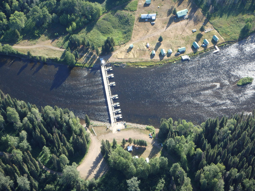 An aerial photo shows a river with buildings on either side and a structure spanning the river.