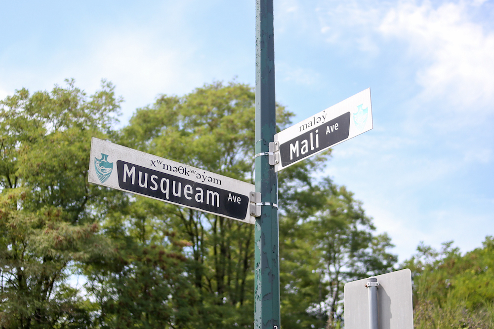 Street signs on a sunny day with Musqueam Ave and Mali Ave in English and accompanying hən̓q̓əmin̓əm̓.