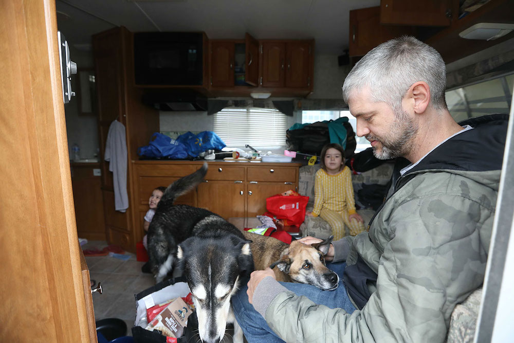 Two dogs, two girls and a man in a cluttered trailer.