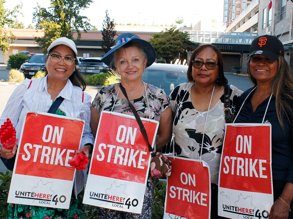 People smile at the camera wearing signs that say ‘On Strike.’