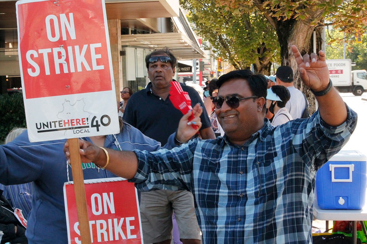 People smile at the camera holding signs that say ‘On Strike.’