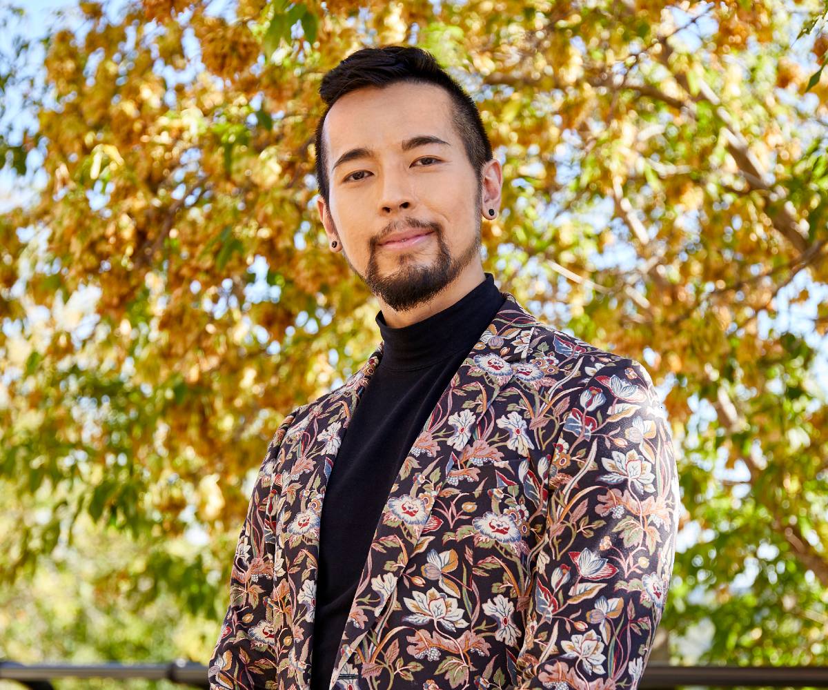 A person wearing a floral blazer stands outside, under a tree, in autumn.