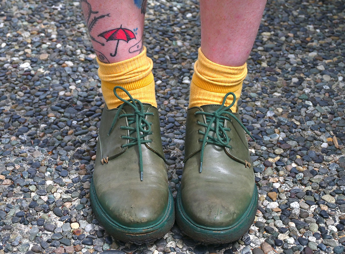 A close up of Alex’s green leather shoes. She has a tattoo of a red umbrella that represents sex worker advocacy. 