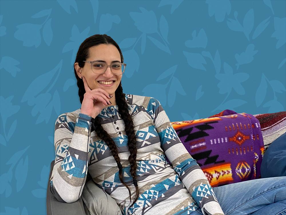 A person with braids sits on a couch. The background is an illustration of flowers, with a blue overlay. 