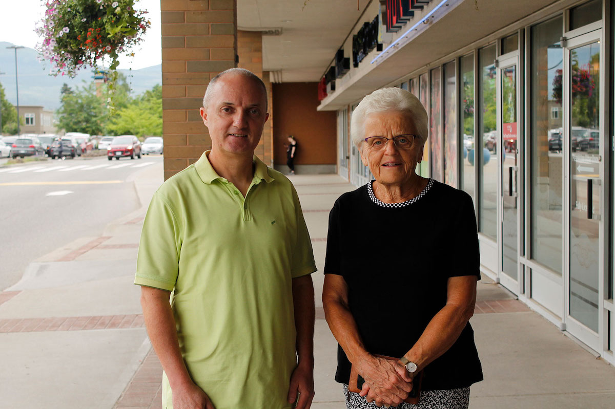 A woman and a man stand on the sidewalk of a shopping plaza.