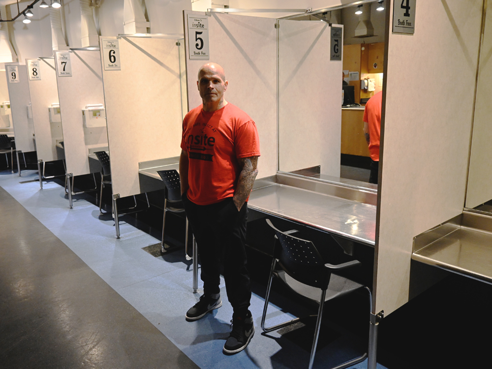 A man wearing an orange Insite shirt stands in front of a booth at Insite.