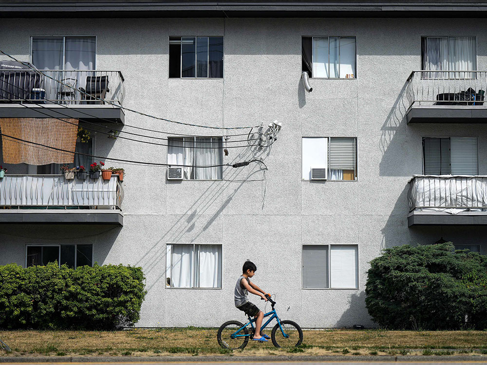 A boy on a bicycle rides past an older apartment building.