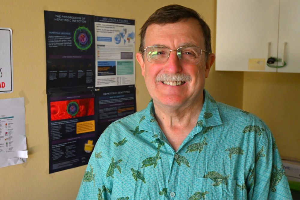 A man wearing a rumpled collared short-sleeved shirt with sea turtles on it smiles at the camera.