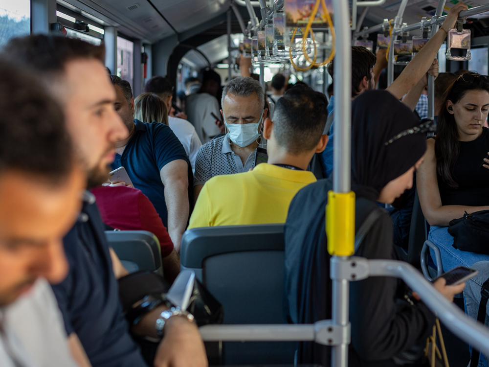 People take a crowded bus. One person is visibly wearing a mask, but most people aren’t.