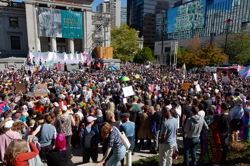 A large crowd gathers in front of the Vancouver Art Gallery, holding placards and rainbow flags.