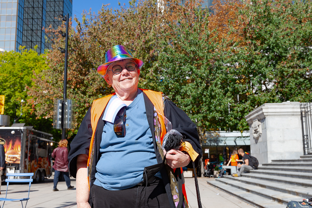 A person wearing a rainbow hat and glasses smiles at the camera.