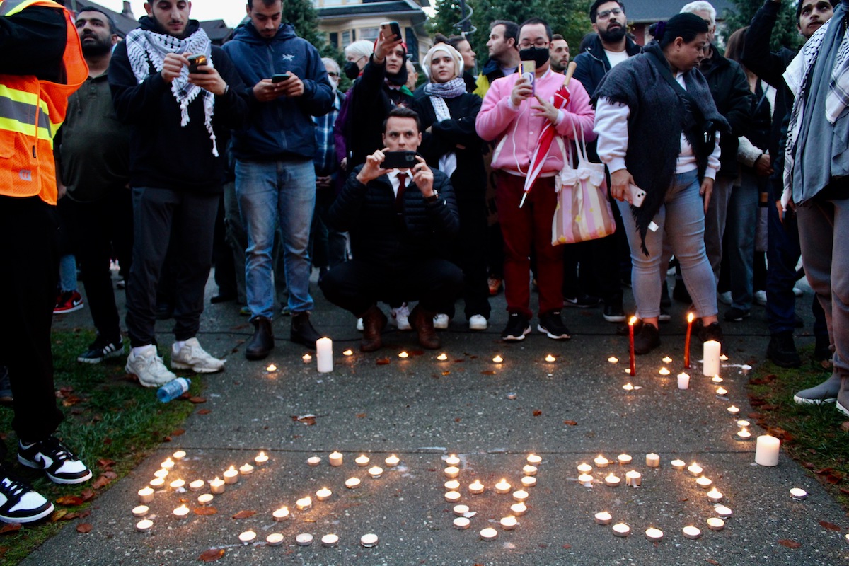 Lit tea lights are organized to spell "GAZA." People gather around. It’s twilight, and getting rainy.