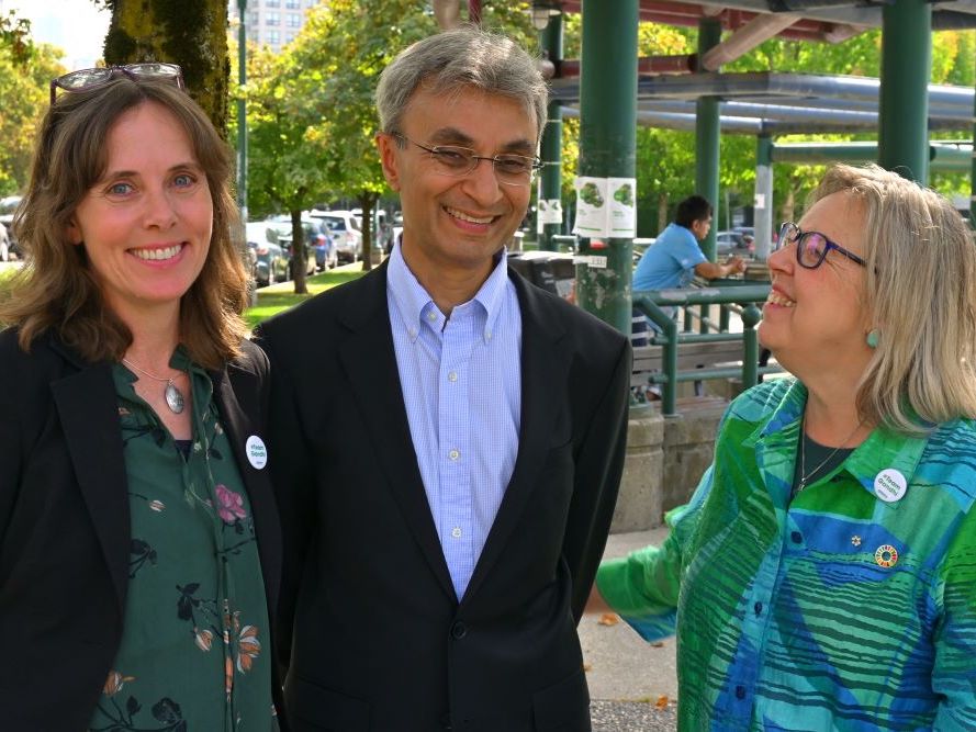 From left to right, Sonia Furstenau, a light-skinned woman with dark shoulder-length hair, Sanjiv Gandhi, a brown-skinned man with short dark hair and glasses, and Elizabeth May, a light-skinned woman with grey-blond hair and glasses, pose for a photo.