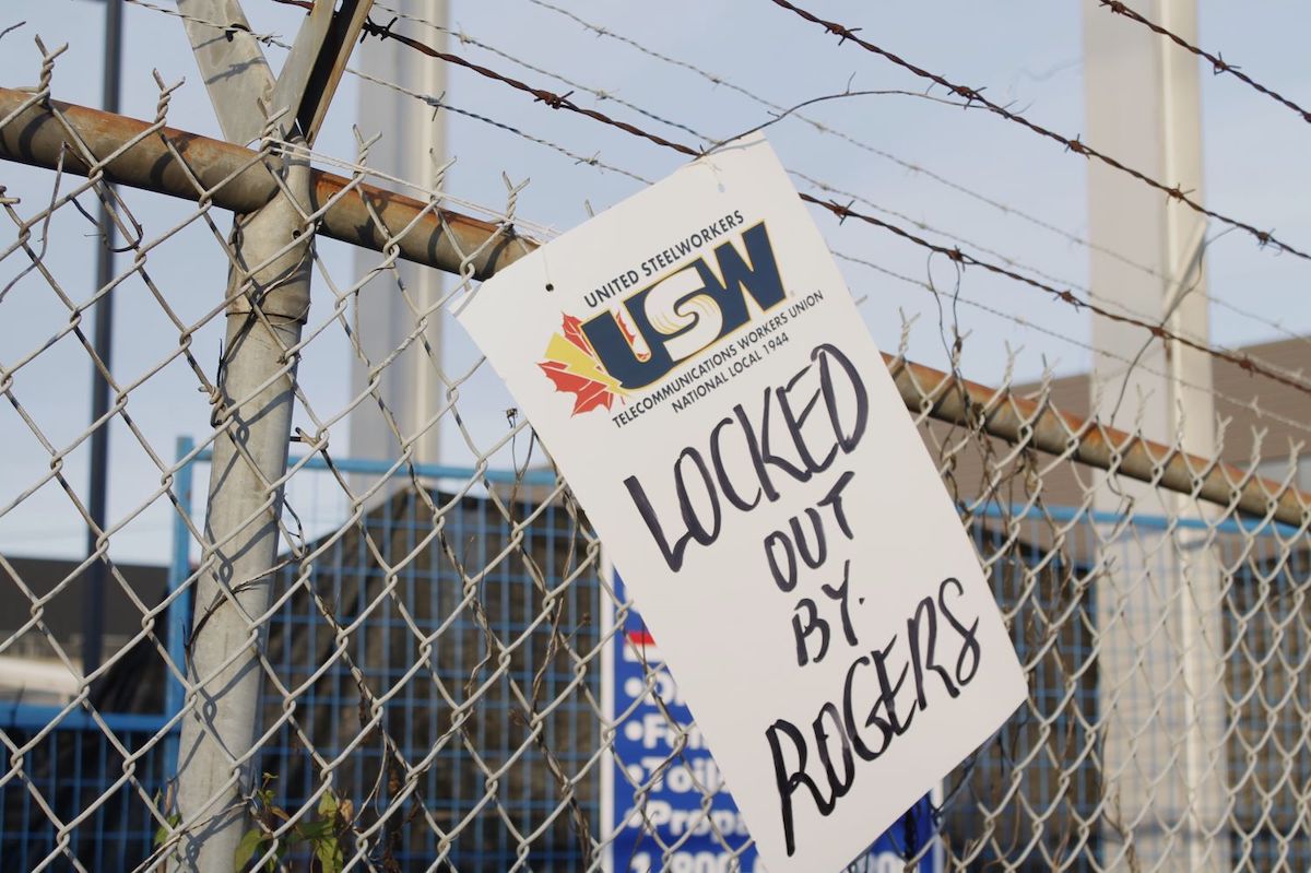 A sign on a chain-link fence topped with barbed wire says 'United Steelworkers' and 'Locked Out by Rogers.'