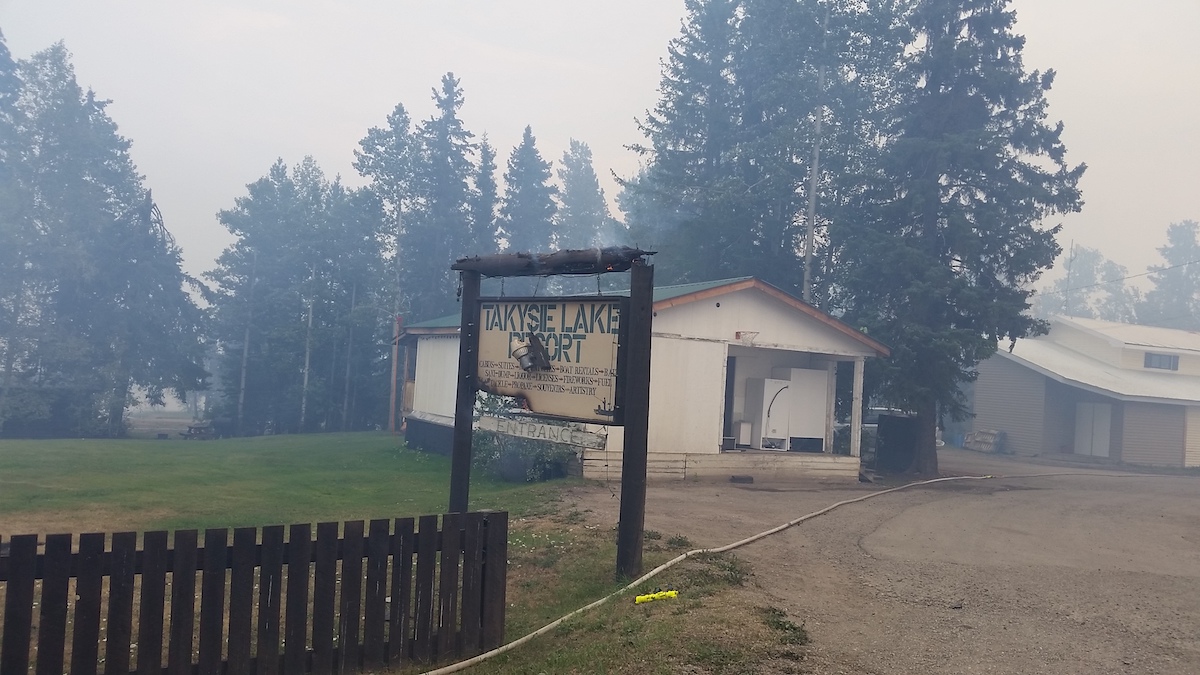 A sign that says Takysie Lake Resort smoulders in an area with trees and cabins. The air is very smoky.