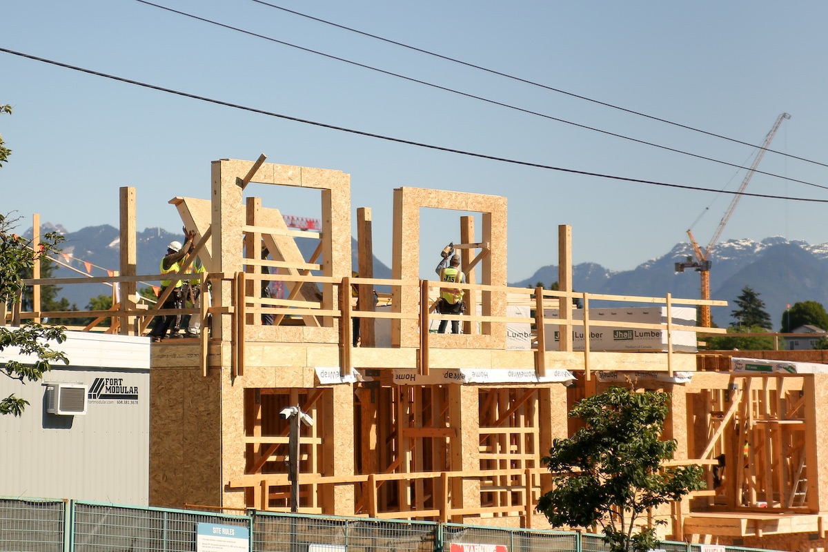 Construction workers standing on the frame of a mid-rise with the mountains in the back.