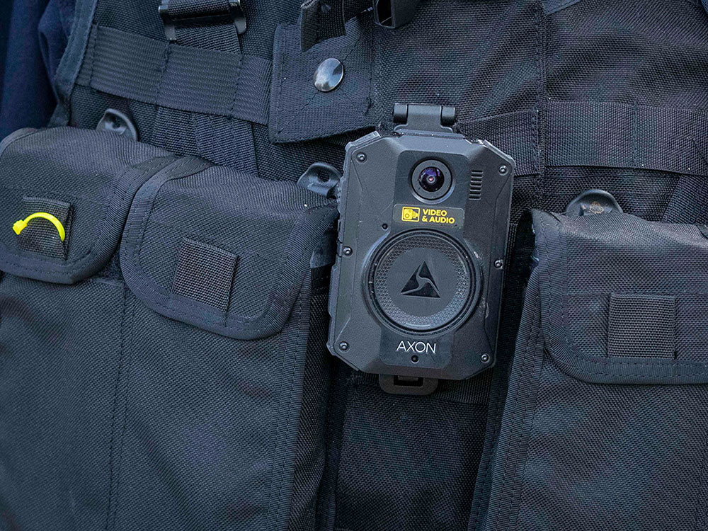 A close-up of a police officer’s chest, with a video camera attached to their other gear.