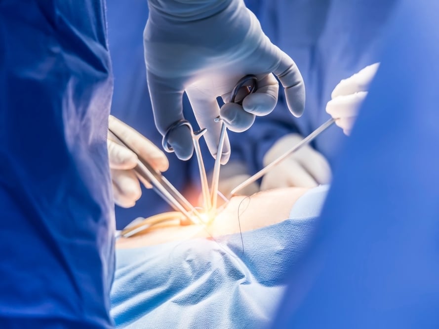 A bright light is trained on a spot where hands are using surgical tools in an operating room.