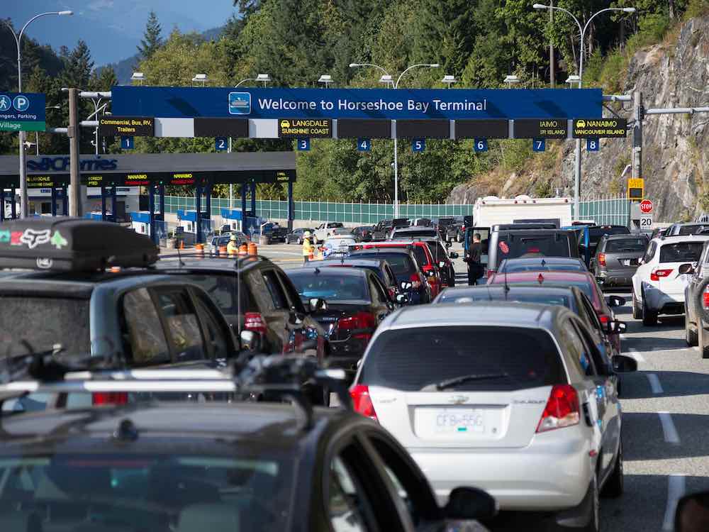 Lines of cars wait to reach the ferry toll booths. A large sign says ‘Welcome to Horseshoe Bay Terminal.’
