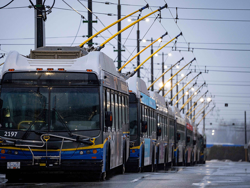 A parked row of TransLink buses stretches into the distance under grey skies.