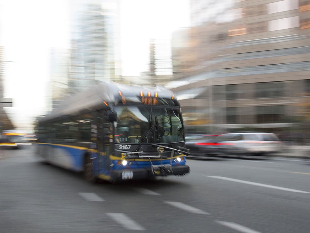 A bus, medium blue with a yellow strip below the windows, drives along a street. The photographer has created a blurry and stylized effect.