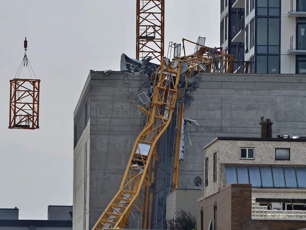 A small building in the foreground, with a larger concrete building under construction and the twisted yellow metal ruins of a crane.