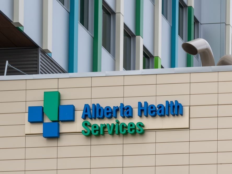 The blue and green 'Alberta Health Services' logo on beige tiles on the side of an institutional building.
