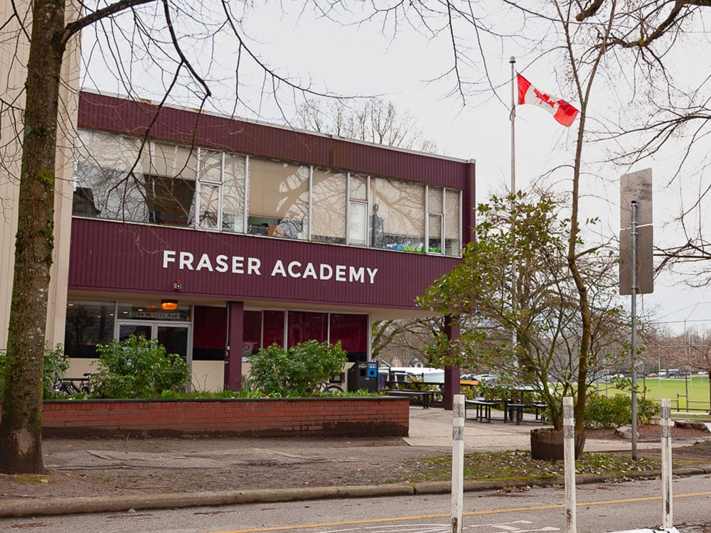 A burgundy building next to a park. Letters on the building read, 'Fraser Academy.'