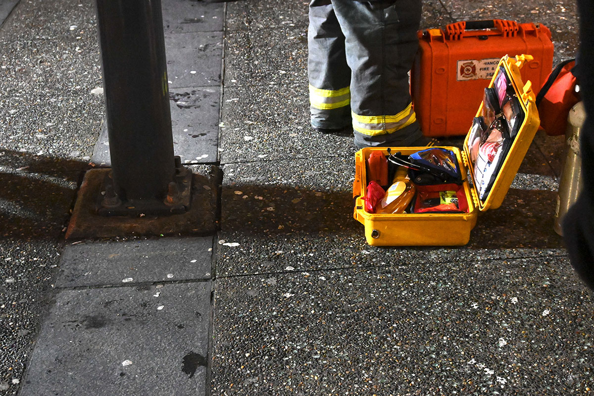 A yellow health kit is open on the ground. The pant cuffs of a firefighter are visible in the background.