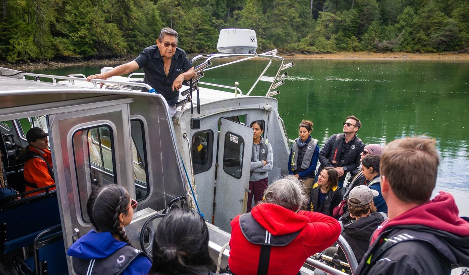 A man speaking to a group of people aboard two boats, side by side in Clayoquot Sound.