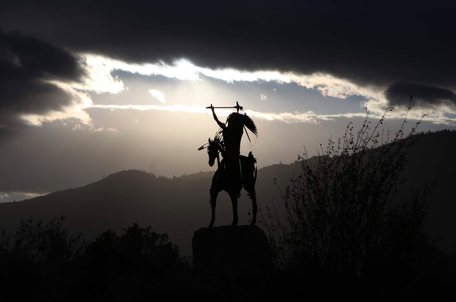 Nk’Mip Desert Cultural Centre, a statue of a Chief on horseback, with the sun peeking beneath dark clouds