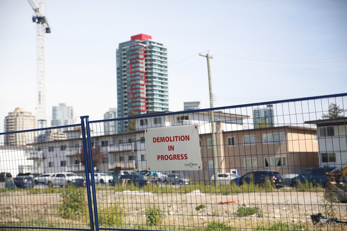A construction fence holds a white sign that reads 'Demolition in progress' in red text. Behind it are highrise condo towers.