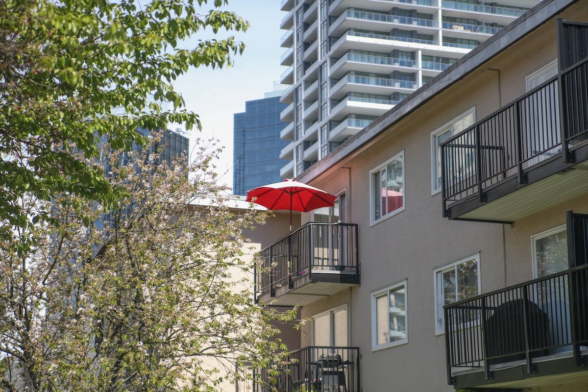 A low-rise beige apartment building features a red patio umbrella on one balcony.
