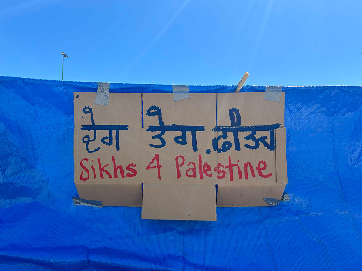 A photo of a handwritten sign that says 'Sikhs for Palestine' is taped to a blue tarp.