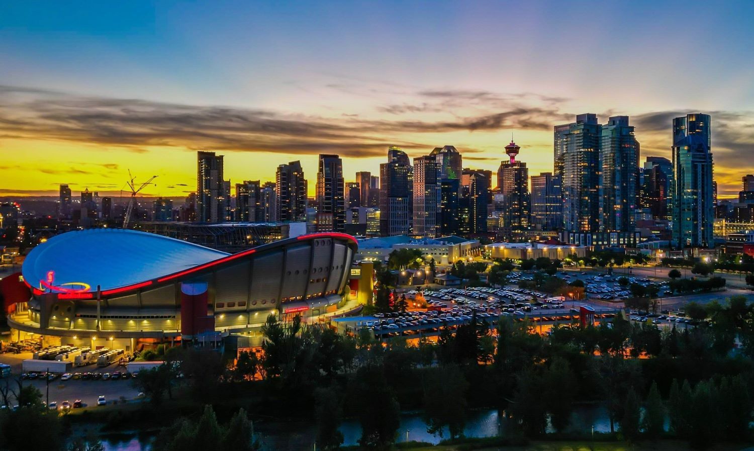 A view of a bright downtown landscape at sunset features an arena with a white saddle-shaped roof.