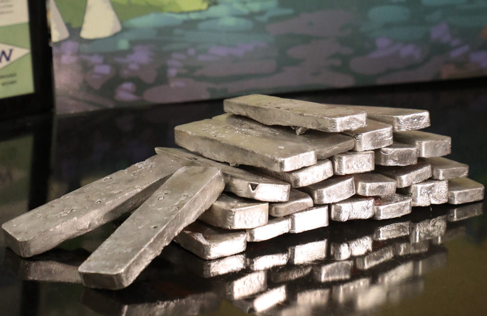 Shiny, skinny ingots lie in a stack on a reflective surface.