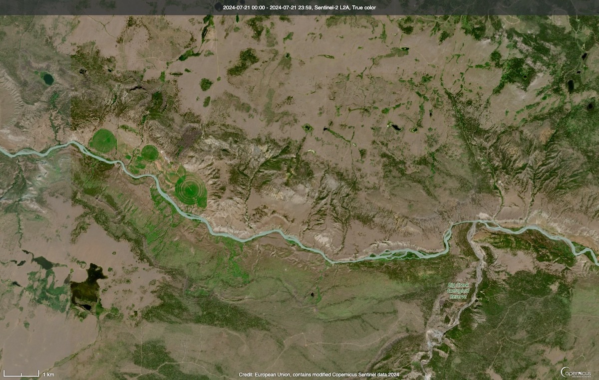 A satellite image shows a blue-green river wending through a brown and green landscape.