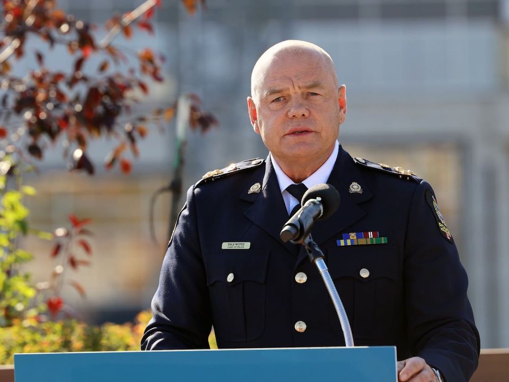 A bald, middle-aged, light-skinned man in a blue police jacket stands outside in front of a podium.