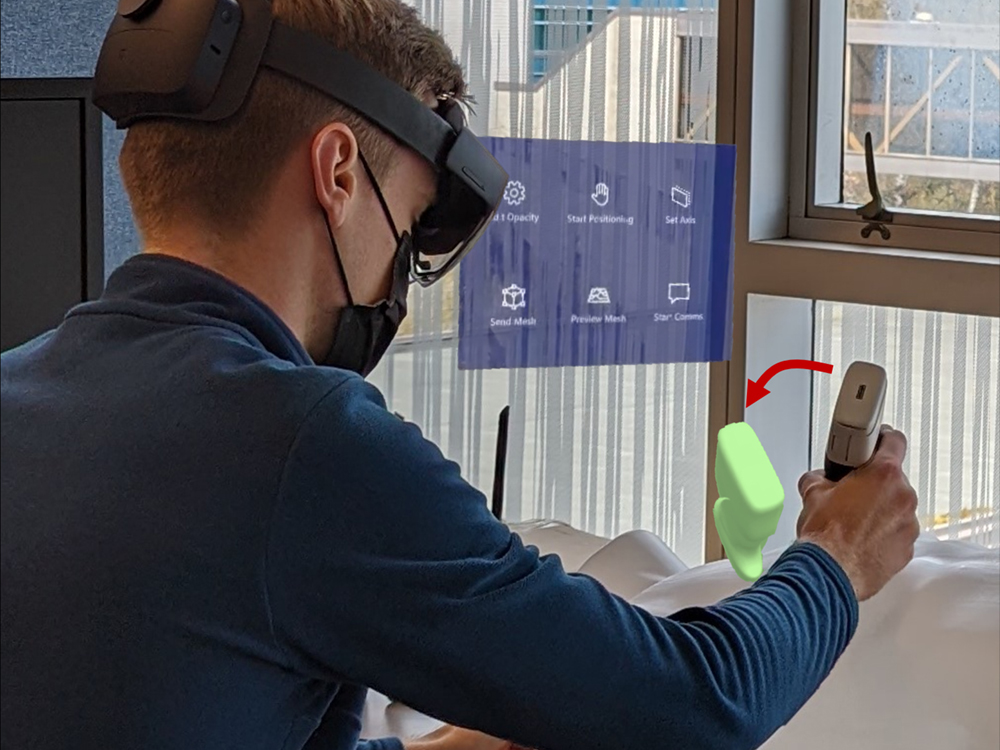 A man wearing a headset leans over a dummy with an ultrasound probe. A hologram appears to the left of the ultrasound probe.