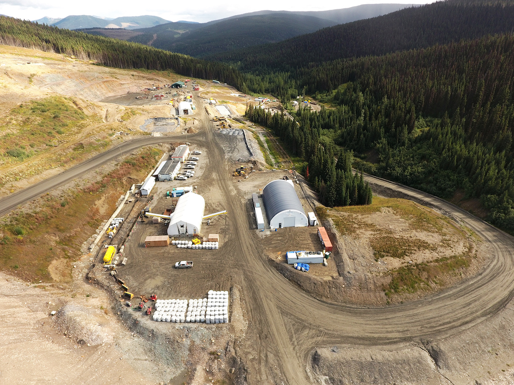 An aerial photo shows a large swath of cleared land, with several structures and rows of parked vehicles.