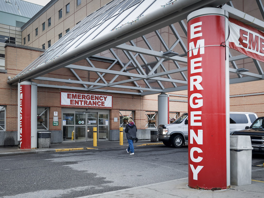 The emergency room entrance at Peter Lougheed hospital in Calgary, with large signs and a person walking in a crosswalk.