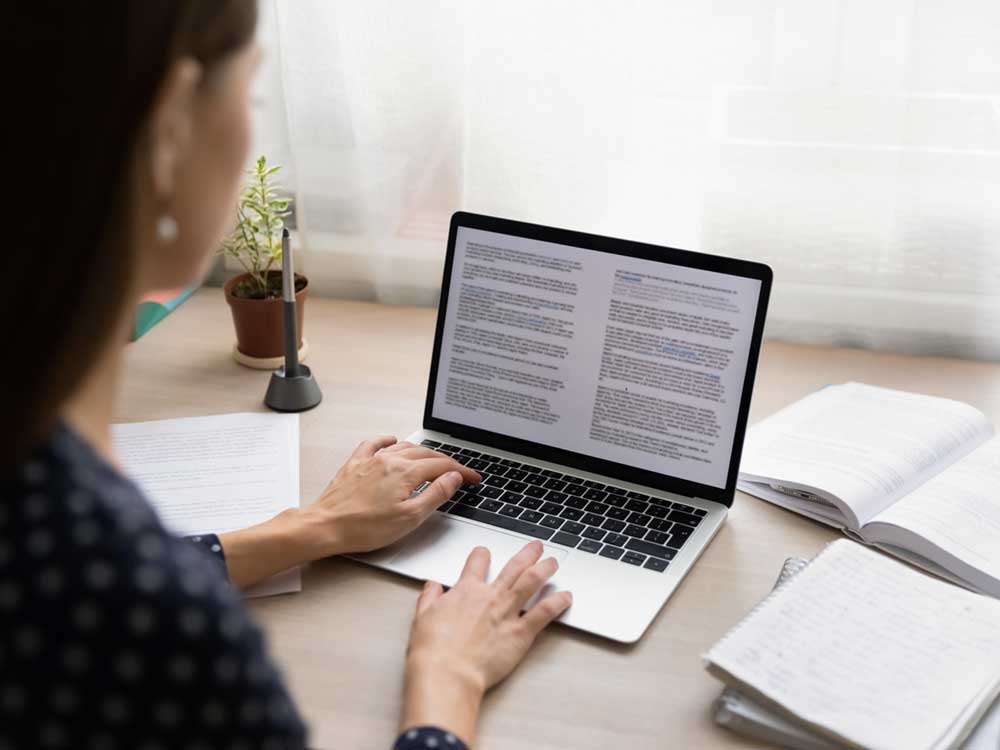 A photo of a person with long dark hair and a light skin tone reading through documents on their computer. 