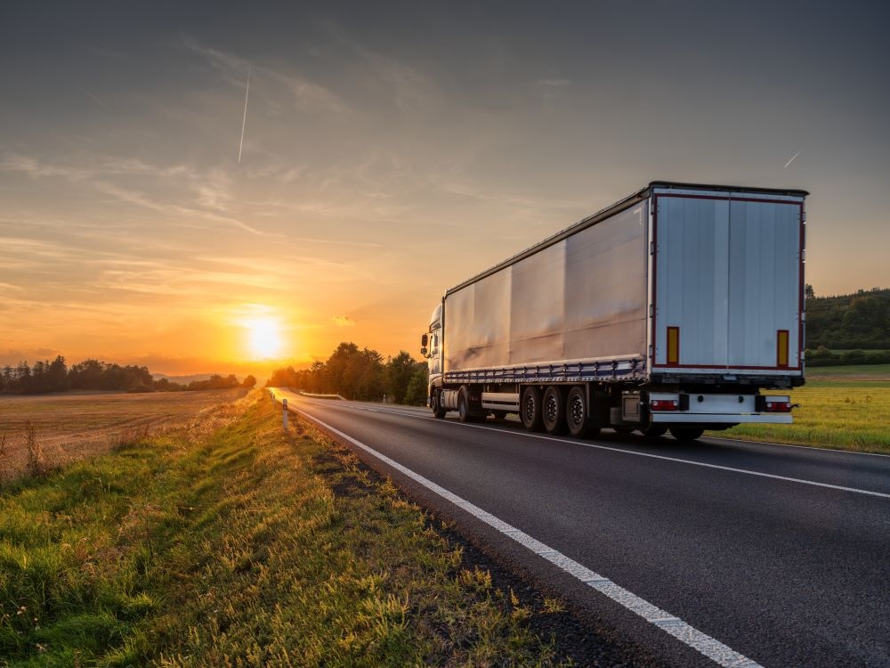 A semi-trailer truck drives into the sunset.